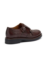 Scarpa brogue in pelle marrone con doppie fibbie, perforazioni decorative, punta arrotondata e suola in gomma nera.
