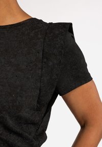 Zwarte top met korte mouwen en een gestructureerde, licht glanzende afwerking. Kenmerkend zijn de gestructureerde schouderaccenten en subtiele versieringen.