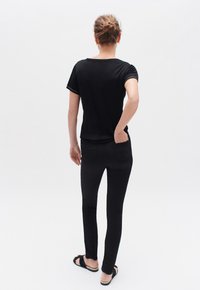 Camiseta negra de manga corta con cuello redondo, combinada con pantalones negros ajustados. El conjunto tiene una textura suave y un diseño sencillo.