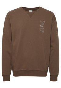 Sudadera marrón con cuello redondo, puños y dobladillo acanalados. Presenta texto bordado en blanco: "TÓMATE EL TIEMPO QUE NECESITES" en el pecho.