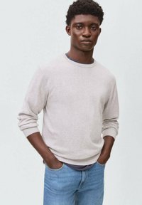 Suéter de punto gris claro con cuello y puños acanalados, combinado con jeans de mezclilla azul, con un corte relajado y un diseño casual.