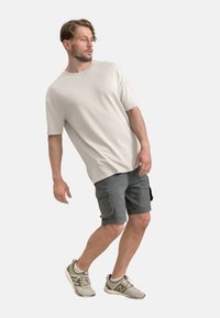 T-shirt oversize grigio chiaro, in tessuto morbido; abbinato a pantaloni cargo grigio scuro con tasche laterali; scarpe sportive grigie.