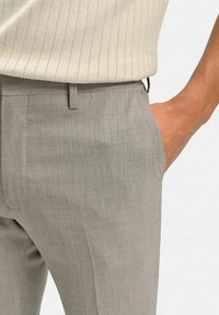 Ljusgråbyxor med en subtil struktur, som har platt front, sidofickor och en smal passform, kombinerat med en ribbad beige topp.