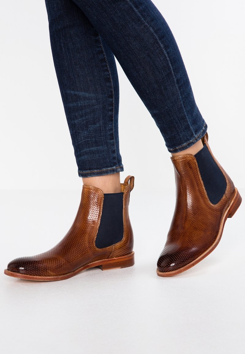 Bottes Chelsea en cuir marron avec motif texturé, panneaux latéraux élastiques et semelles en caoutchouc plates, assorties à un jean bleu foncé.