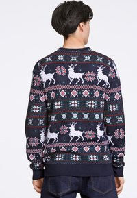 Pulôver de Natal azul-marinho com renas brancas, padrões de flocos de neve e designs geométricos em vermelho e verde. Textura de malha com punhos canelados.