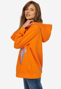 Oranje hoodie met een voorzak, voorzien van een groot blauw grafisch ontwerp en een ribgebreide zoom. Zachte, katoenen stof.