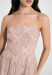 Trägerloses Kleid in zartem Rosa, mit einem strukturierten Muster aus Pailletten, das ein wellenförmiges Design kreiert, aus glattem Stoff und mit figurbetonter Silhouette.