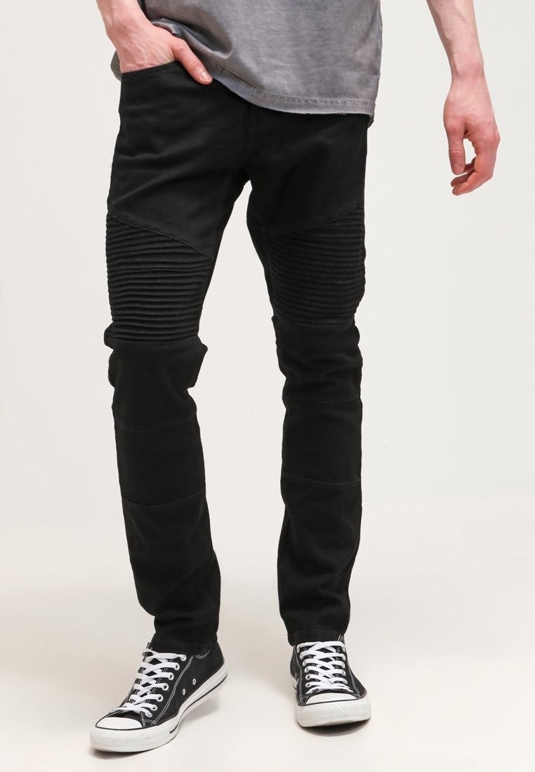 Jeans de mezclilla negra con textura acanalada en las rodillas, de corte ajustado y un acabado ligeramente desgastado, combinados con zapatillas altas negras.