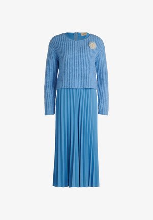 Hellblaues Kleid mit einem strukturierten, gestrickten, kurzen Pulloveroberteil und einem plissierten Rock, akzentuiert durch eine weiße Blumenbrosche auf der linken Brust.
