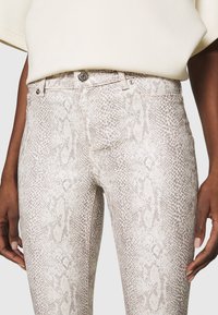 Snakeskin-patterned, light beige pants with a fitted design, front pockets, and silver hardware detailing at the waistband and buttons.