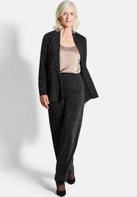 Zwarte sprankelende blazer gedragen over een beige satijnen top, gecombineerd met bijpassende zwarte sprankelende broek en zwarte hakken. Soepele texturen en een op maat gemaakte pasvorm.