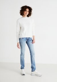 White ribbed sweater paired with light blue jeans and white sneakers. The sweater features a round neckline and long sleeves.