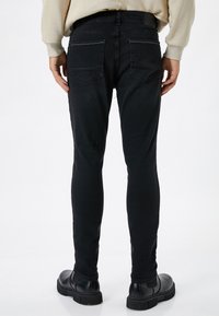 Slim-fit mustat farkut, joissa on sileä pinta, varustettuna takataskuilla ja yksinkertaisella vyötärönauhalla, yhdistettynä mustiin kenkiin.