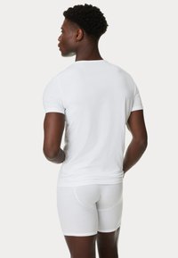 Witte katoenen T-shirt en boxershorts op een persoon, aansluitend ontwerp, soepele textuur, korte mouwen, simpele naden en geen zichtbare patronen.
