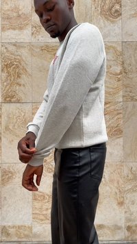 Light gray sweatshirt with ribbed cuffs, worn with fitted black faux leather pants. The background features textured stone tiles.
