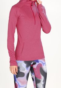 Maglia sportiva a maniche lunghe e cappuccio di colore rosa, con mezza zip, vestibilità comoda e tasca frontale; abbinata a leggings multicolori con motivo ondulato.