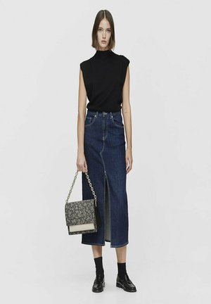 Top negro sin mangas combinado con una falda midi de mezclilla con una abertura frontal. Sosteniendo un bolso con un estampado y una cadena como asa. Zapatos negros y calcetines.