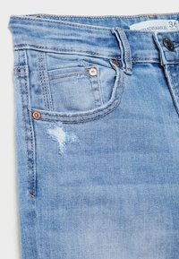 Jeans de mezclilla azul claro con un ligero parche desgastado, diseño clásico de cinco bolsillos, cierre de botón y acentos de hardware en tono cobre.