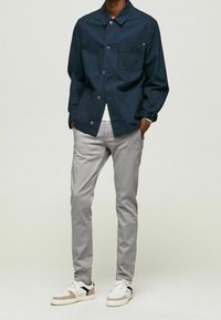 Marineblå knapjakke med brystlomme, kombineret med lysegrå bukser og hvide sneakers med beige og sorte detaljer. Casual outfit.