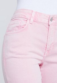 Jeans de color rosa claro hechos de denim, que presentan un diseño clásico de cinco bolsillos, cierre de cremallera y sutiles detalles de desvanecimiento en la tela.