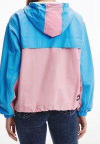 Farveblokjakke med en blå hætte og lyserød nederste del. Lavet af letvægtsmateriale, med elastiske manchetter og en logomærkat i siden.