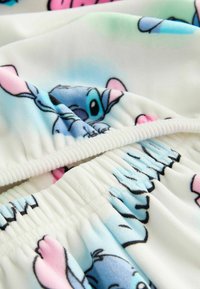 Fleece-pyjamaer med en tegneseriefigur i blå og pink, med elastisk talje og hvid baggrund, der viser en glat tekstur og livlige farver.