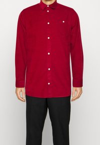 Czerwona koszula na guziki z długimi rękawami, kieszenią na piersi i białymi guzikami. Charakteryzuje się miękką tkaniną i klasycznym kołnierzykiem.