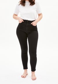 Jeans skinny negros de cintura alta, hechos de denim, con cierre de botón, trabillas para cinturón y dobladillo a la altura del tobillo. Diseño liso, sin patrones visibles.