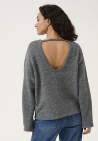Gray, loose-fitting sweater with a soft texture and a deep V-cut back. Paired with blue jeans featuring back pockets.