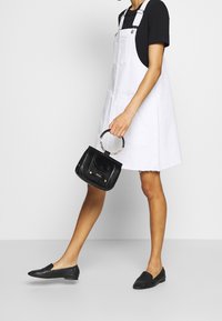 Bílé džínové šaty s rovnou siluetou, nošené přes černé tričko; doplněné černou kabelkou s krokodýlím vzorem.