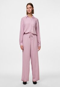 Chemise boutonnée à manches longues de couleur rose clair avec une poche, assortie à un pantalon large avec taille élastique et cordon de serrage.