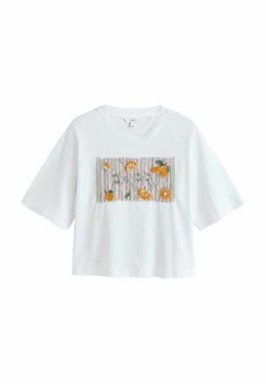 Hvid kort T-shirt med korte ærmer med broderede appelsinskiver og blade på en lyserød og grønstribet rektangulær lap.