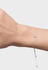 Pulsera de plata que presenta una delicada cadena con una pequeña piedra preciosa transparente y un acento de bola de plata colgante. Textura suave y diseño ligero.