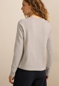 Maglione grigio chiaro a maniche lunghe con polsini e orlo a coste. Tessuto morbido; design minimalista con scollatura arrotondata.