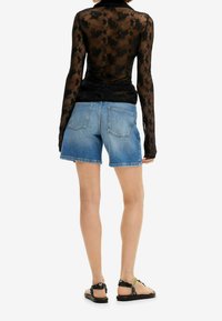 Top negro transparente de manga larga con estampado floral, combinado con pantalones cortos de mezclilla azul claro y sandalias negras con tiras de colores.