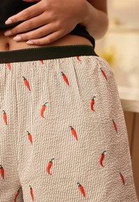 Lightweight cotton pajama shorts with red chili pepper embroidery on a white and gray striped pattern. Features a black elastic waistband.