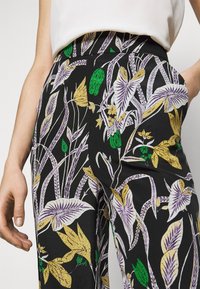 Svarta blommiga byxor med livfulla mönster i lila, gult och grönt, med en slät tygtextur och en skräddarsydd passform.