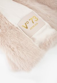 Interno di un cappotto di pelliccia sintetica rosa chiaro con rivestimento in satin crema, caratterizzato da un'etichetta stampata in oro che recita "V°73 VENEZIA." Finitura morbida e strutturata.