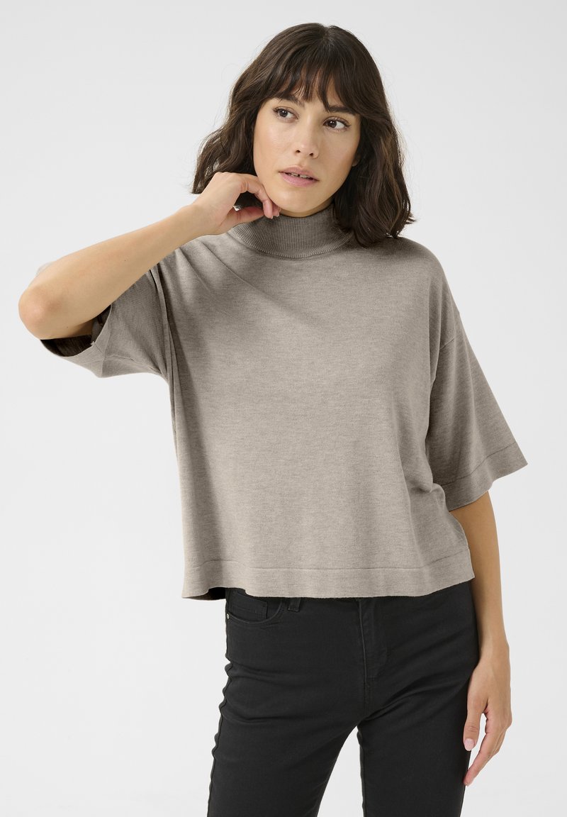 Pull court beige clair avec un col montant, des manches courtes et une texture lisse, associé à un jean noir.