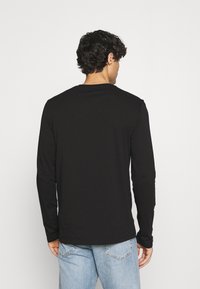 Long-sleeve black shirt made from soft fabric, featuring a crew neck and a straight hem, paired with light-blue denim jeans.