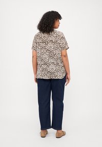 Camicia a maniche corte con motivo paisley marrone e bianco; abbinata a pantaloni a gamba larga blu scuro e ballerine beige.