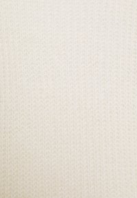 Tissu tricoté crème clair présentant une texture lisse et des mailles fines et régulières, créant une apparence douce et confortable.