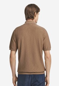 Brun kortärmad polo tröja med strukturerad stickning, ribbad krage och muddar, rak nederkant och avslappnad passform. Bakifrån visad.