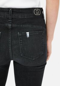 Czarne dżinsy o slim fit, z wysokim stanem i tylnymi kieszeniami. Dekoracyjny logo z kryształów na pasku.