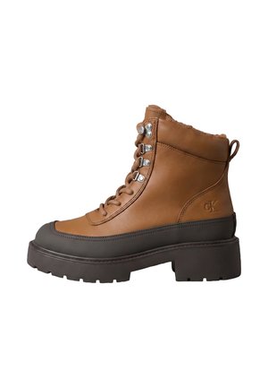Bota de cuero marrón con cordones hasta el tobillo, suela gruesa y oscura y ojales metálicos, con lengüeta para tirar y marca sutil en el lateral.