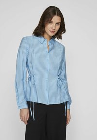 Camisa de botones a rayas azul claro con mangas largas, que presenta detalles de lazo en los lados y un dobladillo recto. Fabricada en una suave tela texturizada.