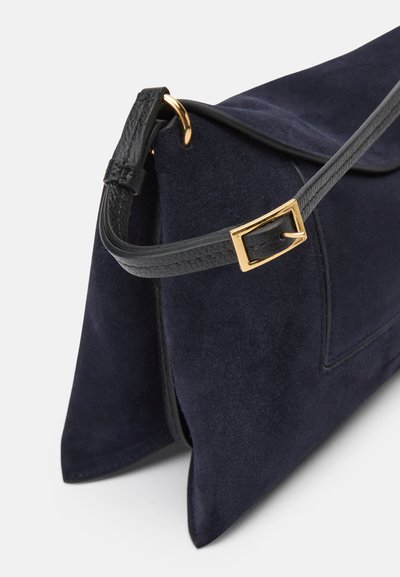 Bolsa de camurça azul-escura com uma alça de couro preta. Apresenta um formato retangular, metalizações em tom de ouro e acabamentos texturizados.