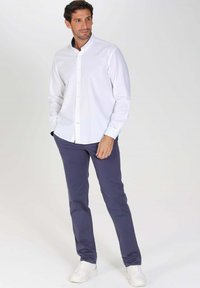 Chemise blanche à manches longues avec boutons, associée à un pantalon bleu marine slim-fit, complétée par des baskets blanches. Tissu en coton lisse, design ajusté.