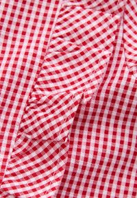 Nahaufnahme von rot-weiß kariertem Stoff mit Rüschendetails und sichtbaren Nähten.