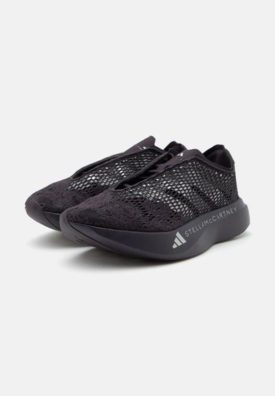 Ζευγάρι μαύρα sneakers slip-on με υφή από δίχτυ και δαντέλα και σήμανση "Stella McCartney" στη χοντρή σόλα, εμφανίζονται με λευκό φόντο.